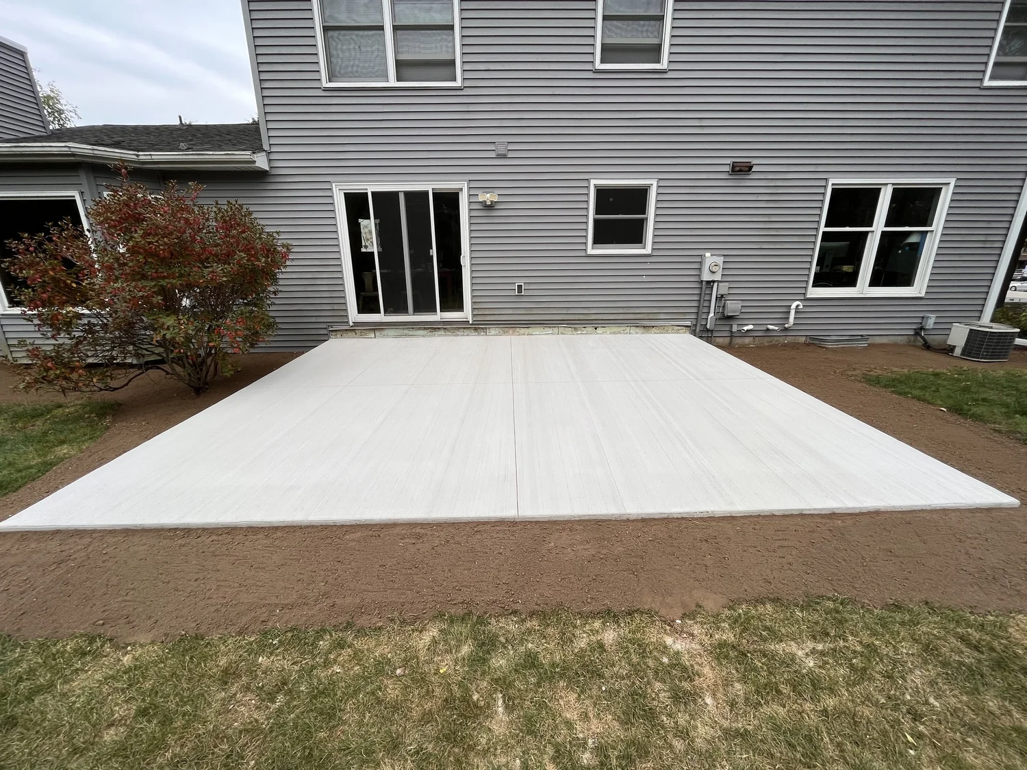 Fresh concrete backyard patio slab poured behind a two-story home